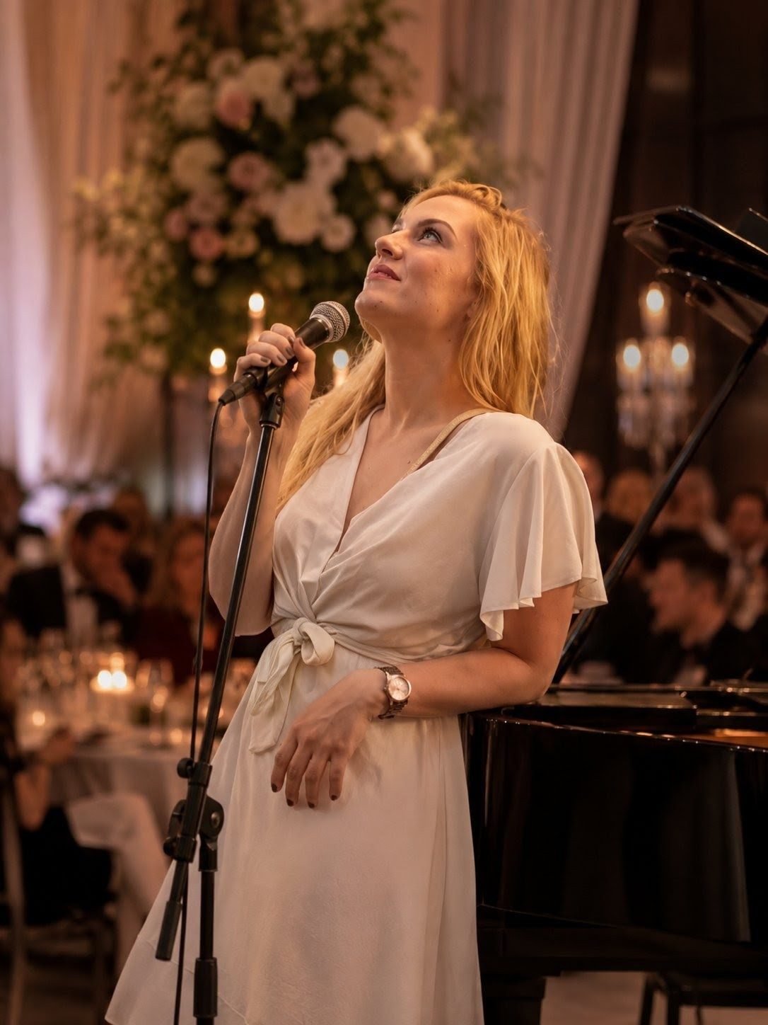 Sara Medić singing beside a grand piano at a candlelit wedding reception